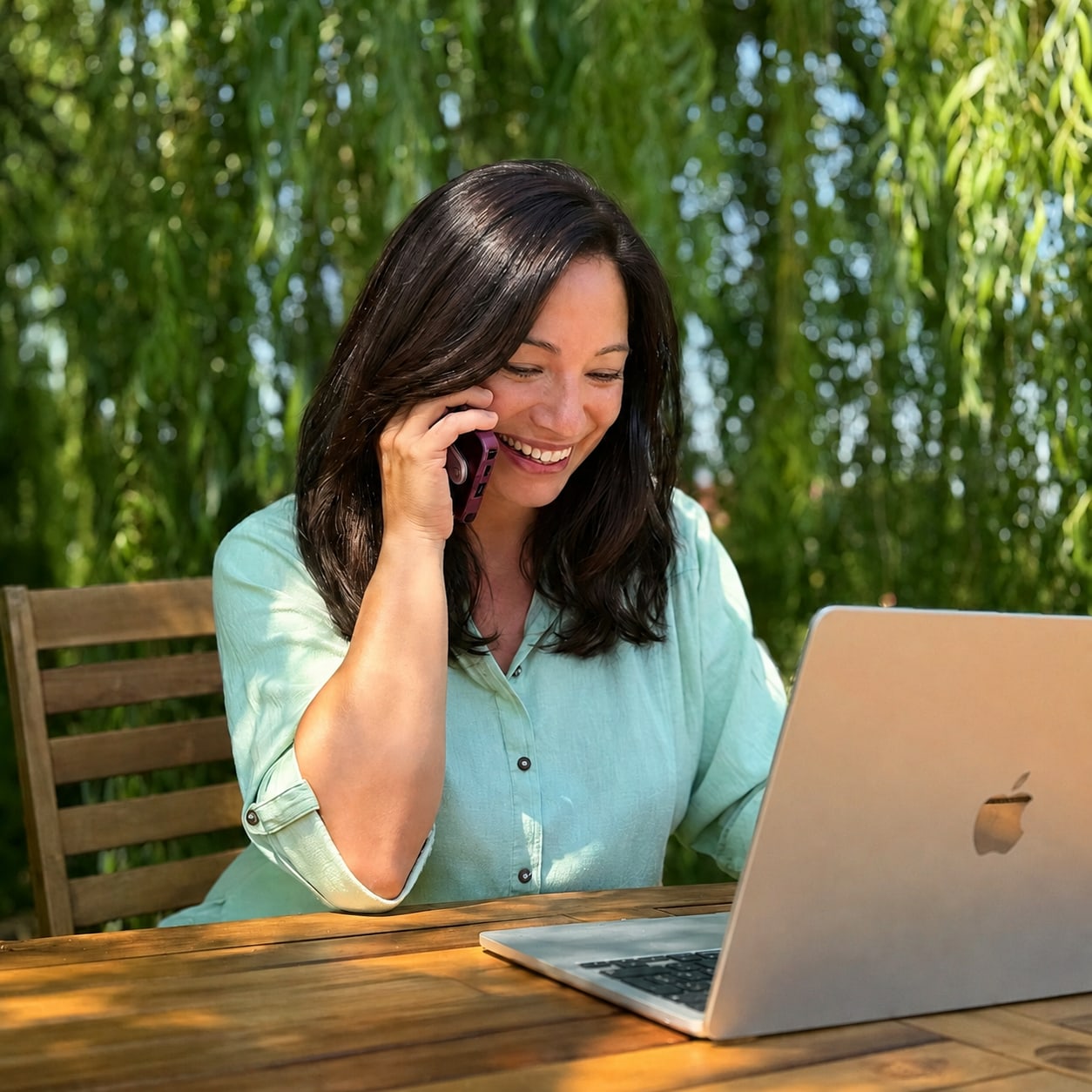 Silvia sorride parlando al telefono davanti al laptop, sotto le fronde di un salice