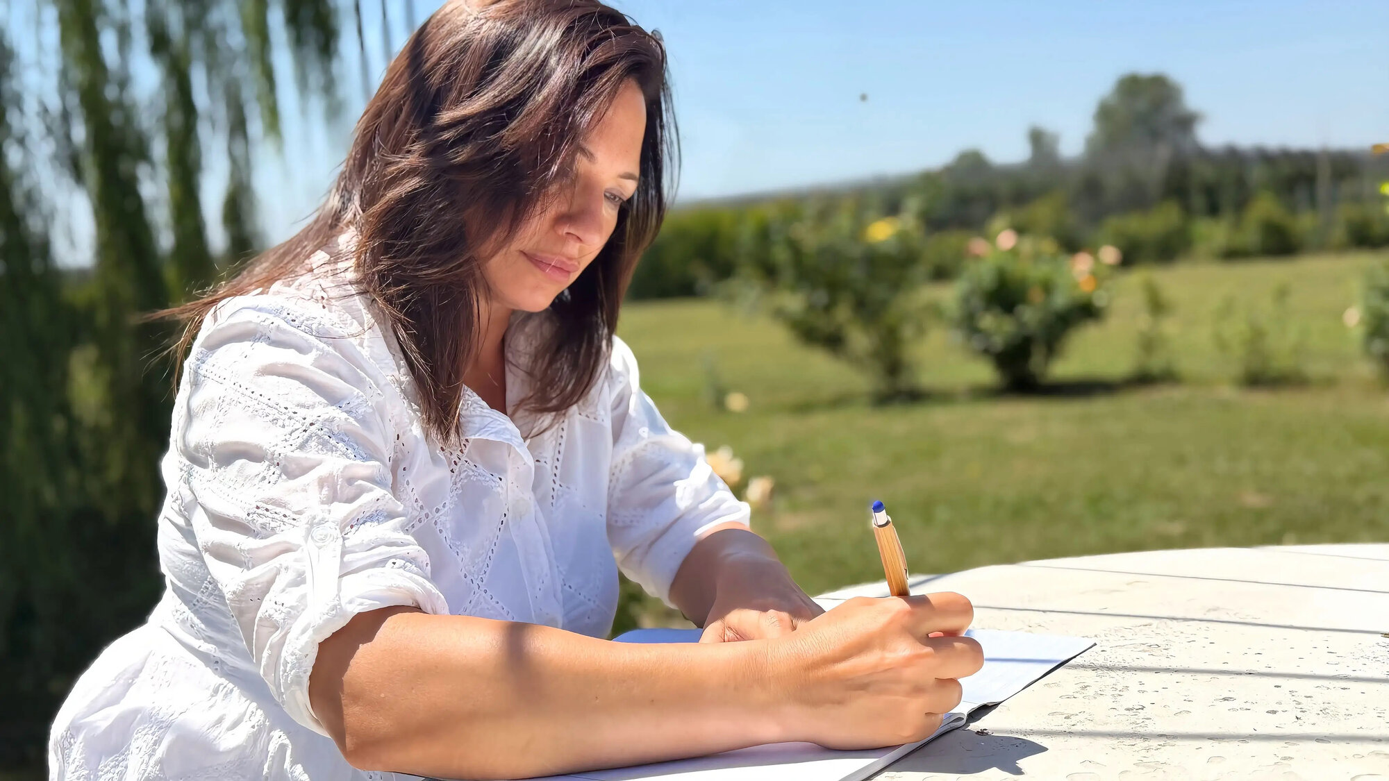 Silvia china sul quaderno studia e annota un itinerario a penna, nel giardino in piena luce