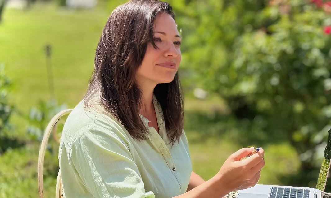 Silvia in ascolto con la penna in mano, il laptop accanto, nel giardino