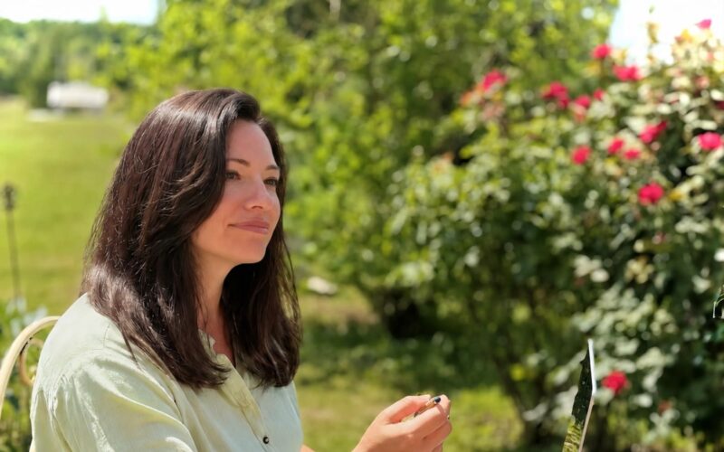 Silvia ascolta un cliente al tavolino del giardino, il roseto alle spalle